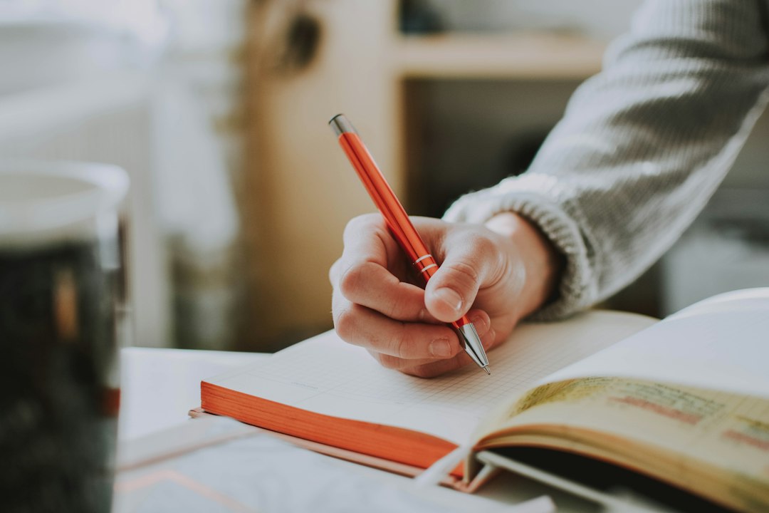 Une main écrit au stylo rouge dans un carnet